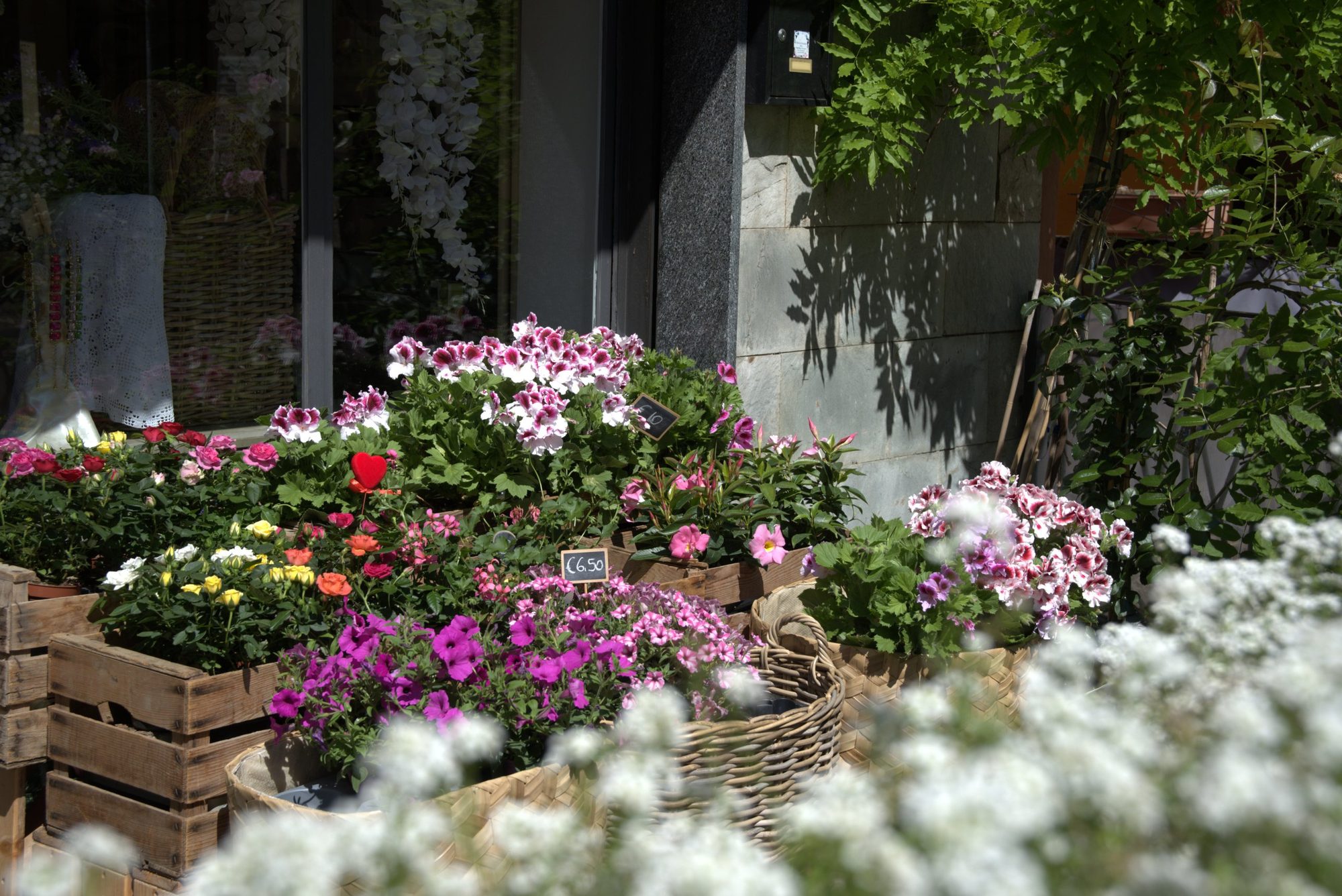 Roses, geraniums and petunias spilling from crates outside a European florist
